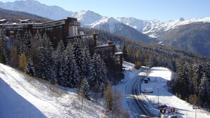 Ein modernes Hotel mit mehreren Etagen, umgeben von schneebedeckten Bäumen und Bergen.