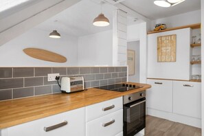 A modern kitchen with a wooden countertop, white cabinets, a built-in oven, and a wall-mounted shelf with glasses.
