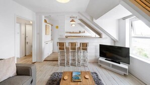 A modern apartment with a TV, a coffee table, and a bar area. - Beach-Style Flat, 2 Min Walk to Tolcarne Beach (Newquay)
