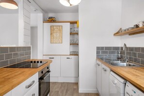 A modern kitchen with white cabinets, a wooden countertop, and a built-in oven. There is a shelf with glassware and a sign that says "Coffee is good idea."