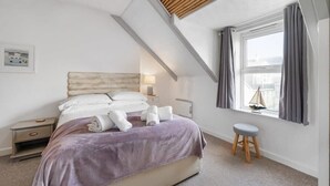 A bedroom with a bed, nightstand, and window with curtains. - Beach-Style Flat, 2 Min Walk to Tolcarne Beach (Newquay)