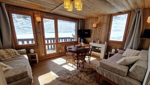 Interior acogedor de una cabaña con paredes de madera, una mesa de comedor, dos sofás y una chimenea.