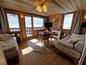 A cozy cabin interior with wooden walls, a dining table, two sofas, and a fireplace.