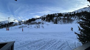 Pista de esquí nevada con esquiadores, cielo despejado y una montaña al fondo.