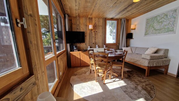 Un interior de madera con zona de comedor, sofá y televisor fijado a la pared.
