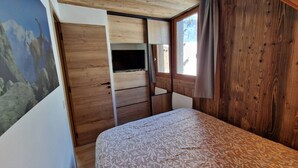 Un dormitorio con cama, armario, televisor y ventana con cortinas.