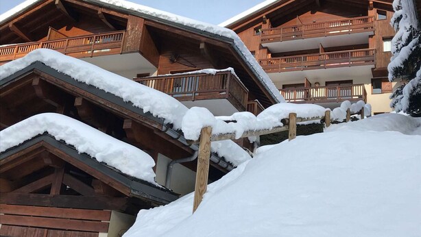 A wooden chalet with balconies, surrounded by snow.