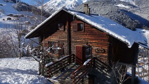 Une cabane en bois, avec un toit enneigé, des fondations en pierre et un escalier en bois menant à un porche.
