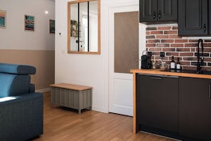 A modern kitchen with dark cabinets, a brick accent wall, and a small dining area with a blue sofa and a wooden table.