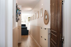 Un pasillo con una puerta de madera, un espejo adosado a la pared y varias fotografías enmarcadas.