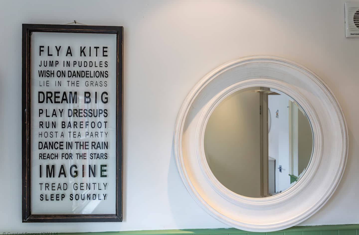 A framed motivational quote on a wall next to a round mirror.