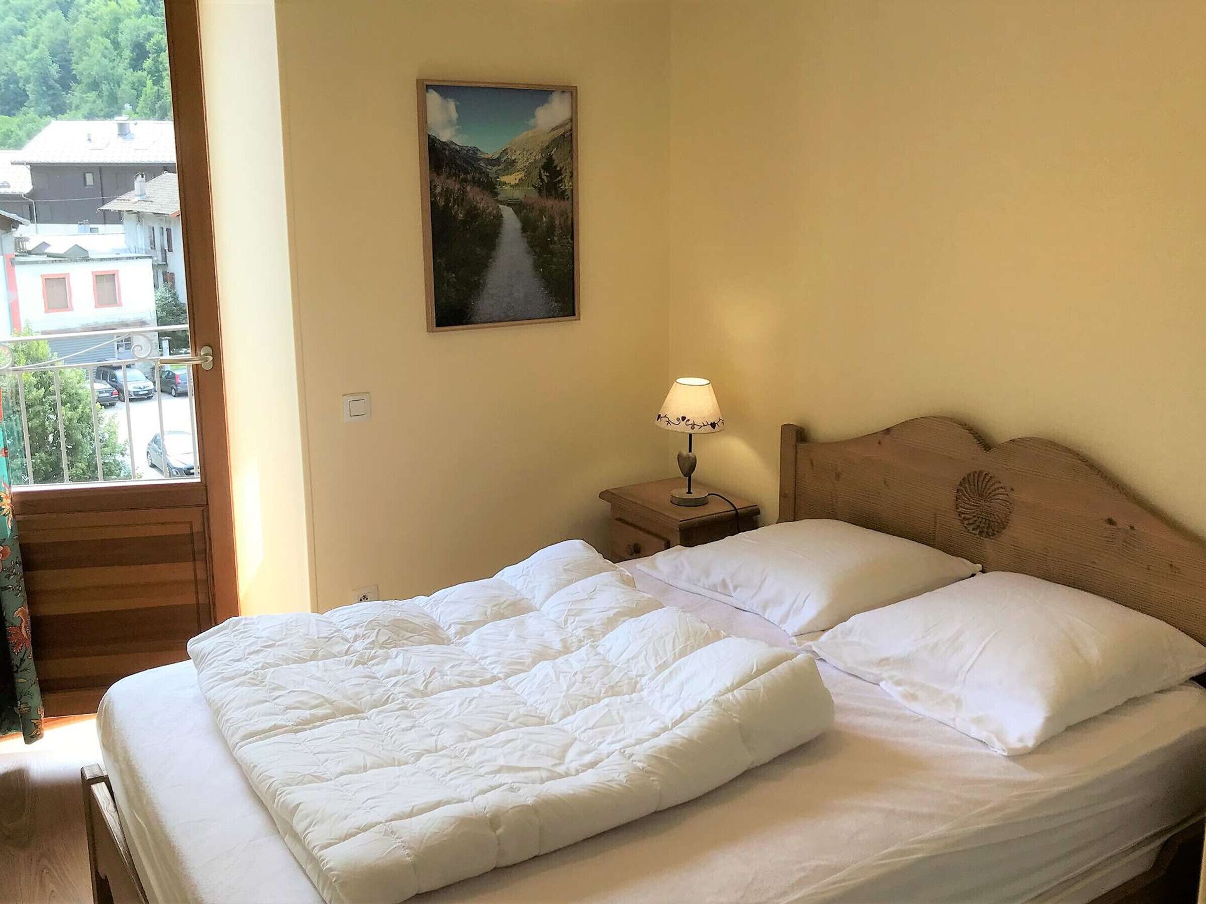 A bedroom with a bed, a nightstand, a lamp, and a painting on the wall.