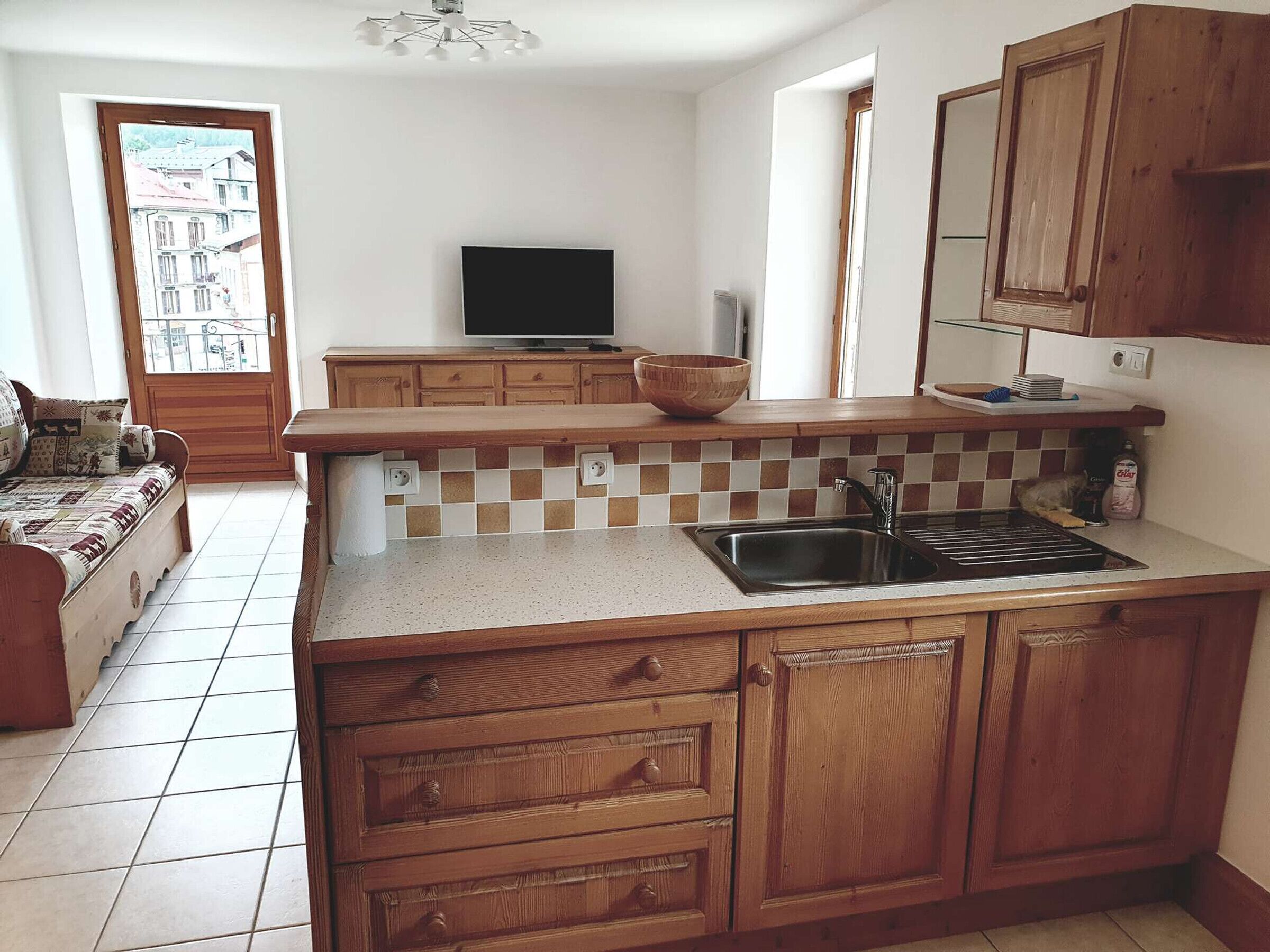 Cuina compacta amb armaris de fusta, salabanc de rajola, vàter integrat i un televisor.