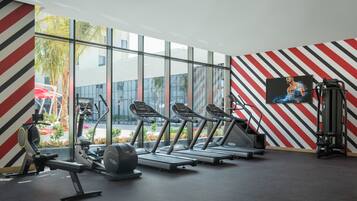 Ein Fitnessstudio mit Laufbändern, einem Kraftgerät und einem großen Fenster mit Blick ins Freie.