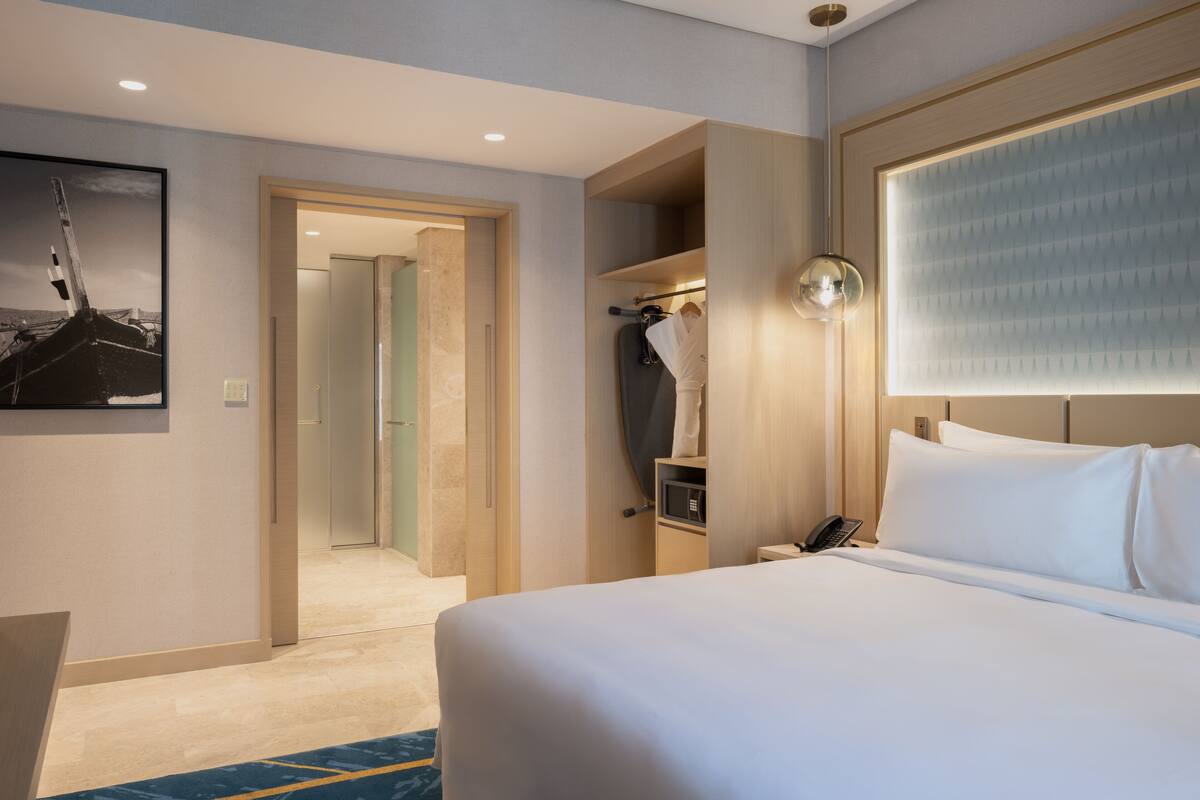 Une chambre d’hôtel avec un grand lit, une armoire, un bureau avec une lampe et un tableau encadré au mur.