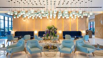 En moderne lobby med blå lænestole, et centralt glasbord og en blomsterdekoration.