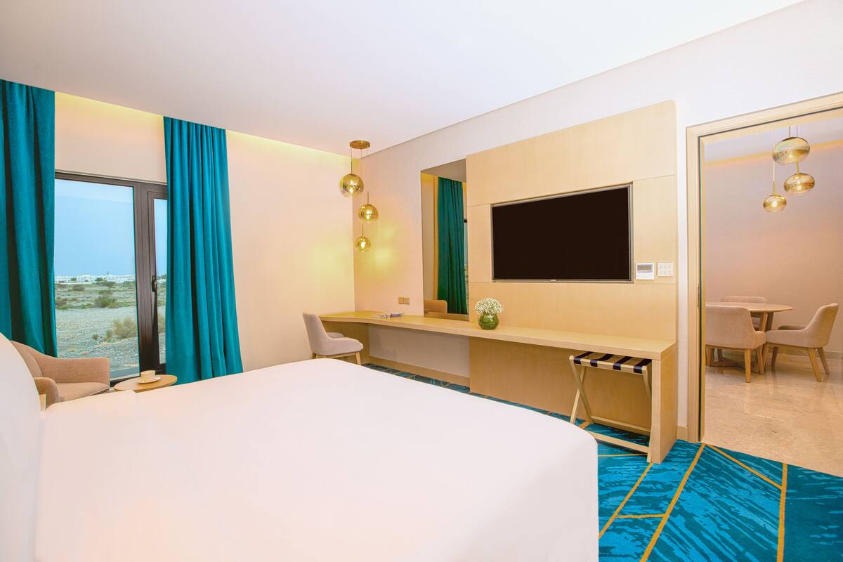 Une chambre d’hôtel avec un grand lit, un bureau, une chaise, une télévision et une petite table avec une tasse.