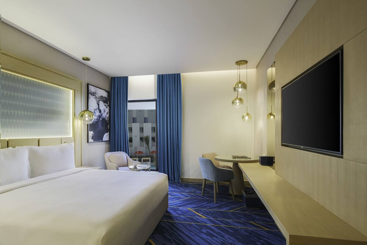 Une chambre d’hôtel avec un grand lit, un bureau avec une chaise, une télévision et une fenêtre avec des rideaux.