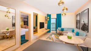 Quarto de hotel moderno com área de refeições, sofá, televisão e vista para o mar.