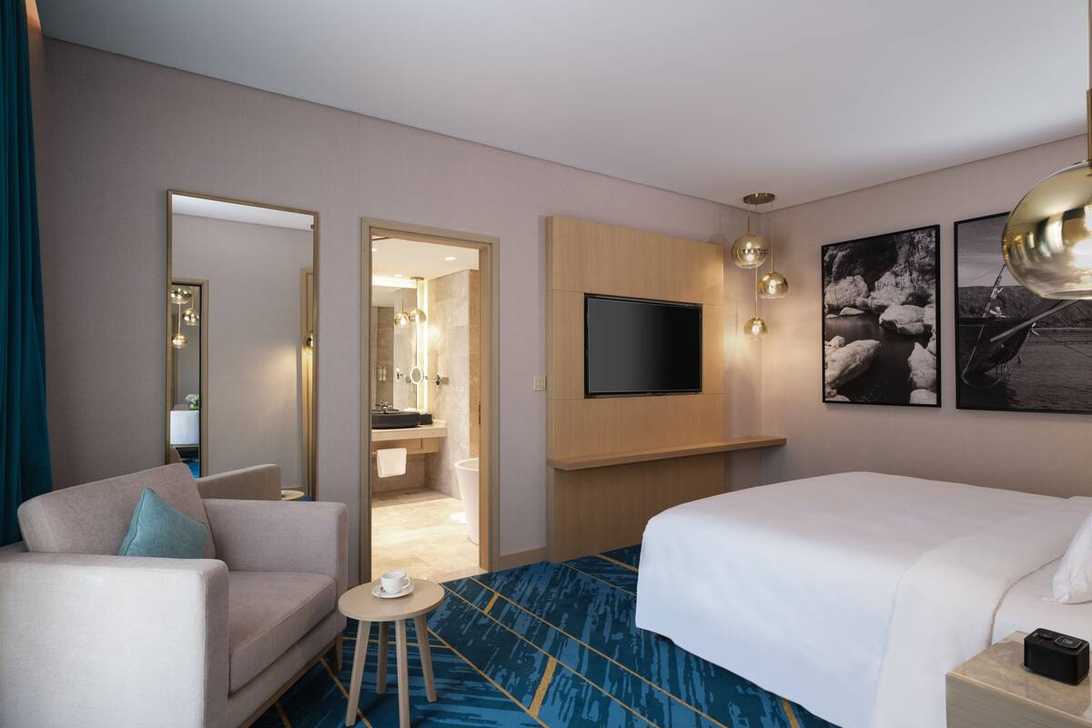 Une chambre d’hôtel avec un lit, un canapé, une petite table avec une tasse, une télévision et un miroir.