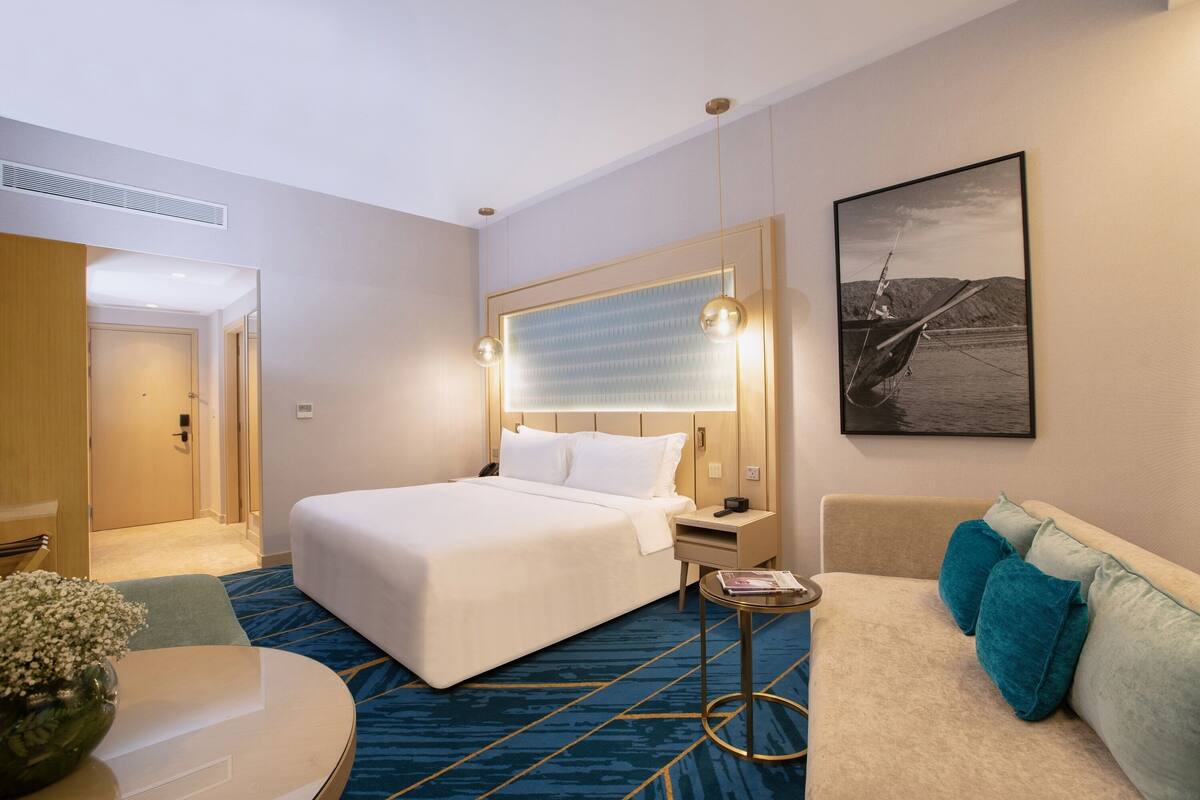 Une chambre d’hôtel avec un grand lit, une table de chevet, une petite table ronde, un canapé et un tableau encadré au mur.