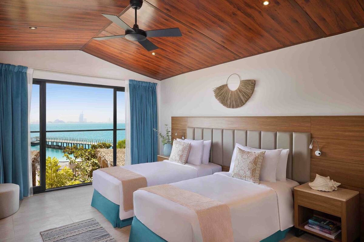 Une chambre d’hôtel avec deux lits, un ventilateur de plafond, une vue sur la mer et un plafond en bois.