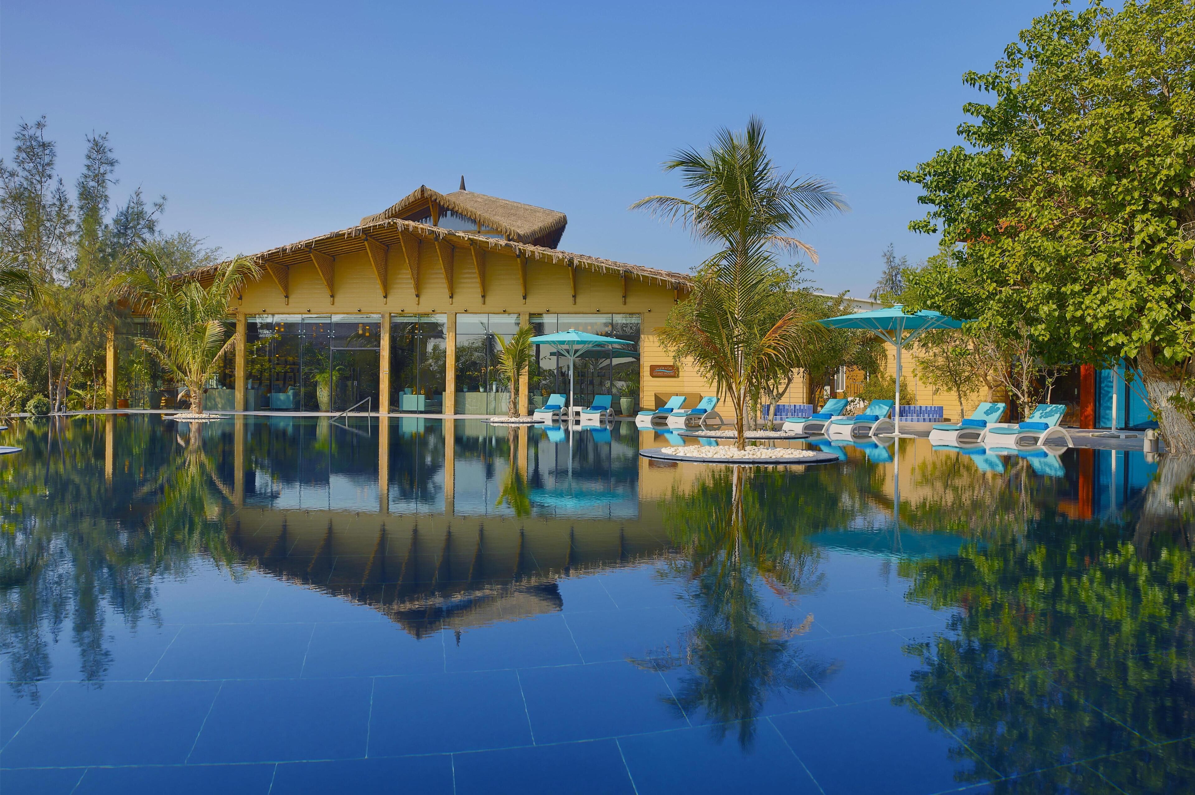 Ein Resort mit Pool, Liegestühlen und einem Gebäude mit einem Reetdach.