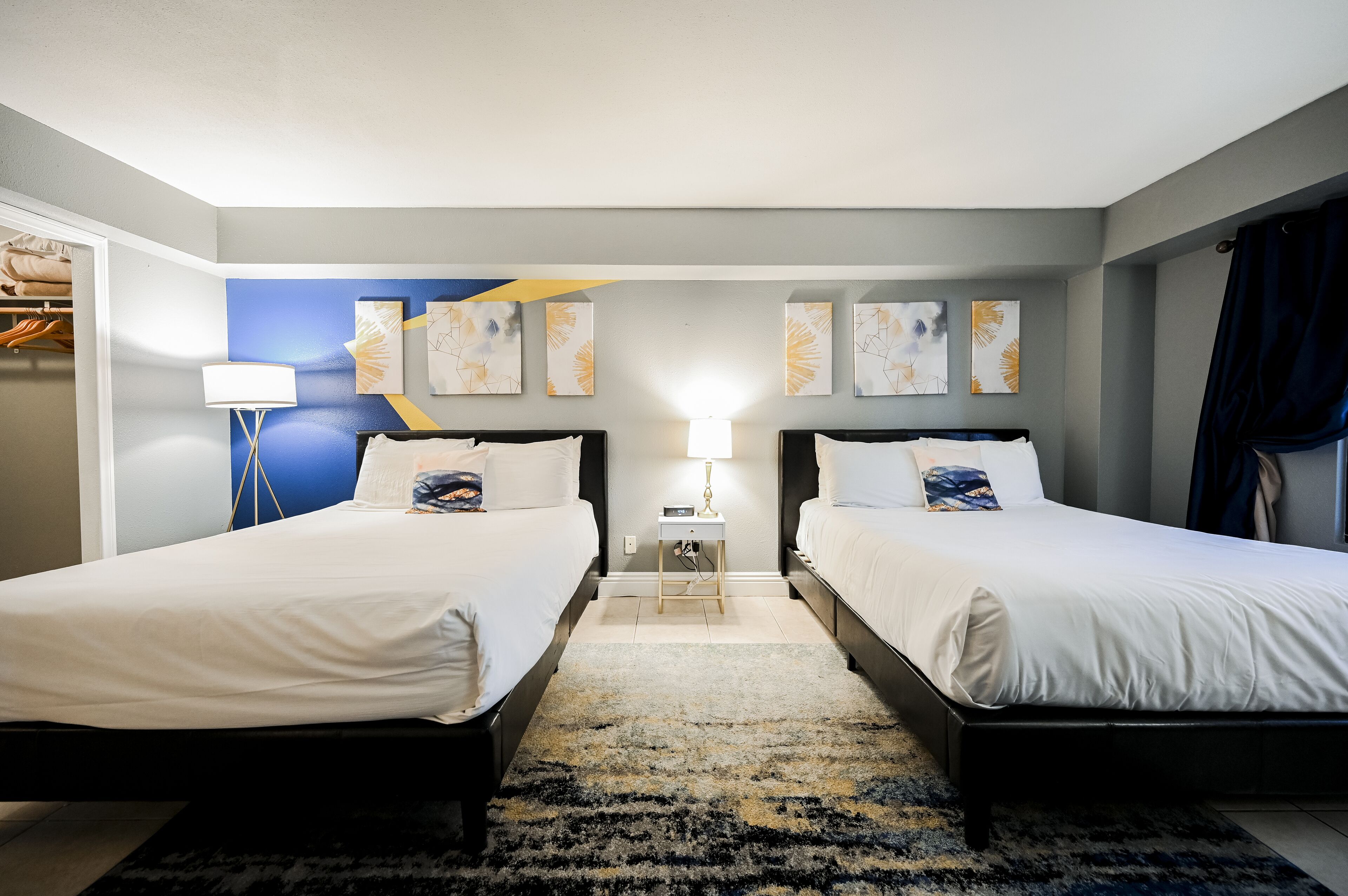 Een hotelkamer met twee bedden, een nachtkastje met een lamp en kunstwerken aan de muur.