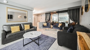 A modern living room with a black leather sofa, a round marble coffee table, and a large mirror. There is a view of a dining area through a glass partition. - SVS: 3BD/3BA Penthouse | 1,600 sqft | Strip Views | Jockey Club (Las Vegas)