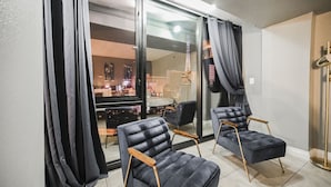 A modern living room with two dark blue armchairs, a glass door leading to a balcony, and a view of a cityscape at night. - SVS: 3BD/3BA Penthouse | 1,600 sqft | Strip Views | Jockey Club (Las Vegas)