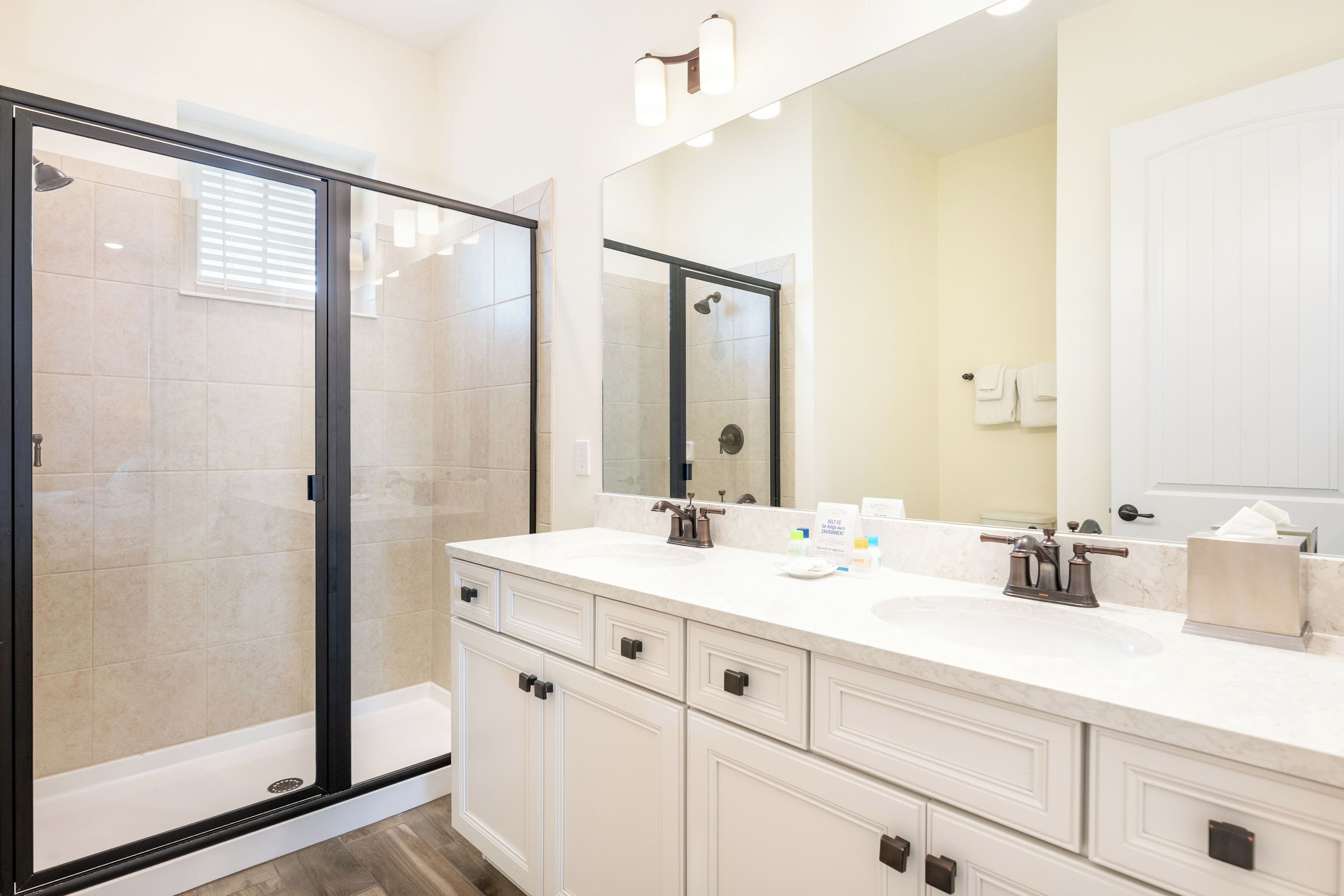 A modern bathroom with a glass-enclosed shower, a large mirror, and a white vanity with multiple drawers.