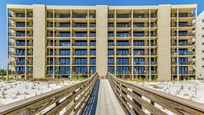 A multi-story hotel with balconies, a wooden boardwalk leading to the entrance, and a sandy beach in the background. - Orange Beach Gulf-View 2BR • Sleeps 8 • Wet Bar • Kid-Friendly • Pools • Boats (Orange Beach)