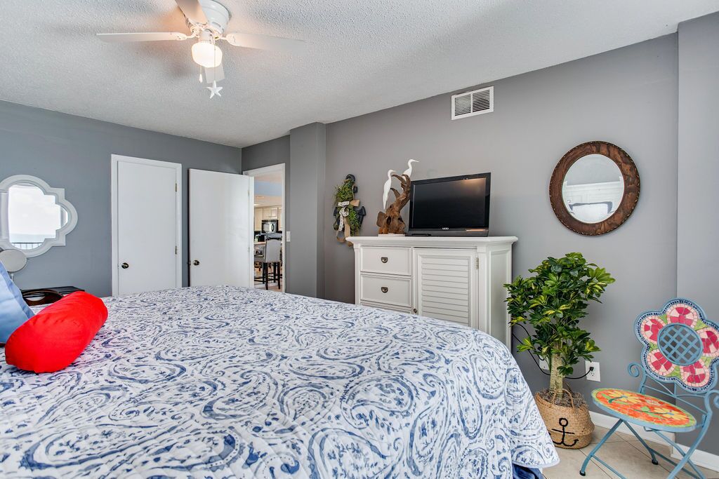 A bedroom with a bed, a television, a dresser, a mirror, and a potted plant.