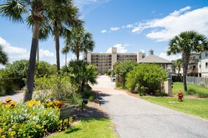 A hotel entrance with a paved driveway, palm trees, and a sign indicating protection by security.