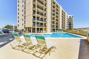 A hotel with a rooftop pool, multiple balconies, and lounge chairs.