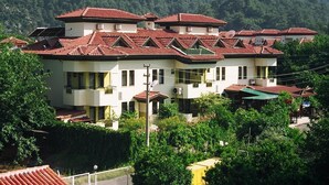 A multi-story building with red-tiled roofs, surrounded by greenery and hills. - Ozay Apart Hotel (Marmaris)