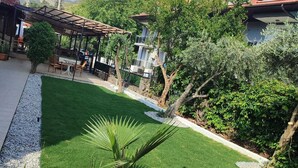 A courtyard with a green lawn, potted plants, a pergola, and a view of a hill with buildings. - Ozay Apart Hotel (Marmaris)