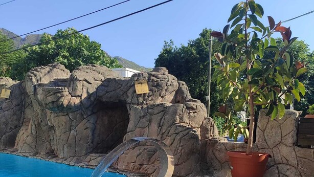 A swimming pool with a waterfall feature, a rock wall, and a potted plant. - Ozay Apart Hotel (Marmaris)