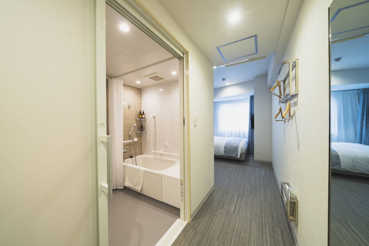 A hotel room with a bathroom, a bed, and a small sitting area.