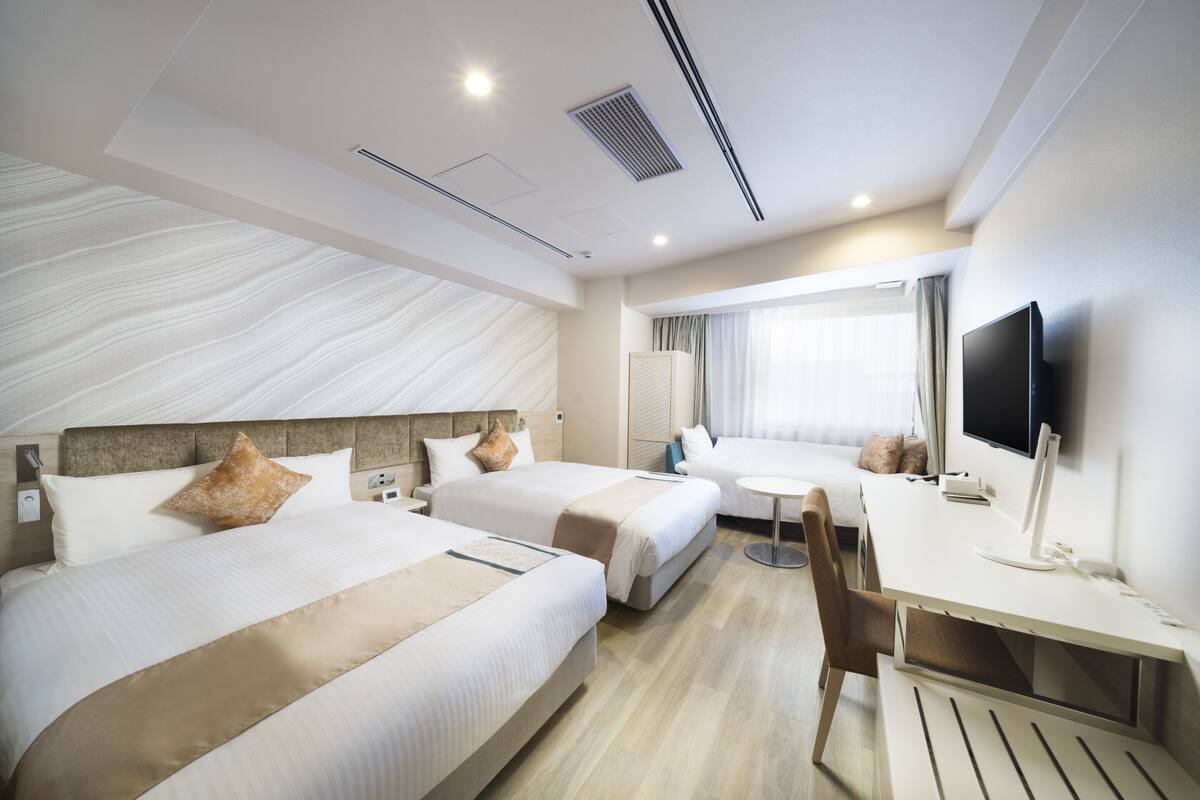 A hotel room with two beds, a desk, a chair, a TV, and a window with curtains.