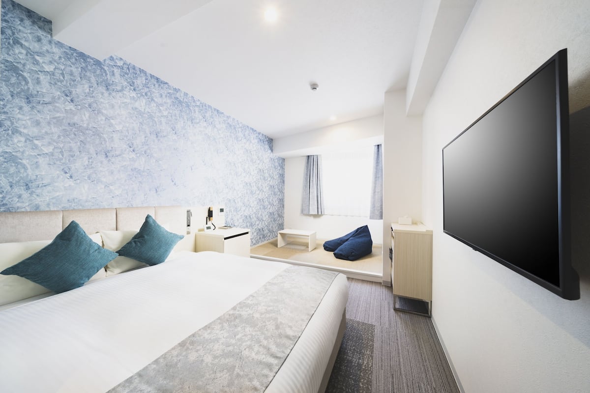 A modern hotel room with a large bed, a flat-screen TV, a small seating area, and a textured wall.