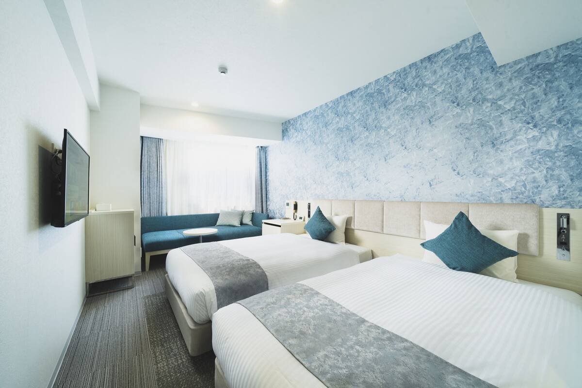 A hotel room with two beds, a sofa, a TV, a bedside table, and a patterned wall.