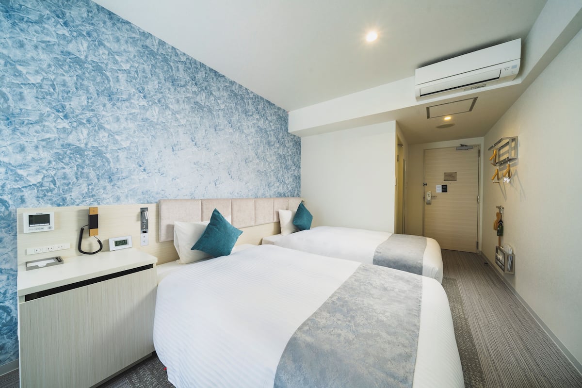 A hotel room with two beds, a minibar, a wall-mounted air conditioner, and a door leading to a hallway.