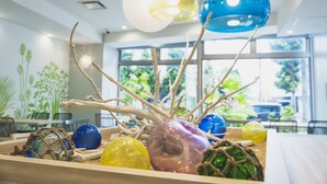 A decorative centerpiece with branches and colorful glass spheres in a well-lit room with large windows. - Rembrandt Style Naha (Naha)