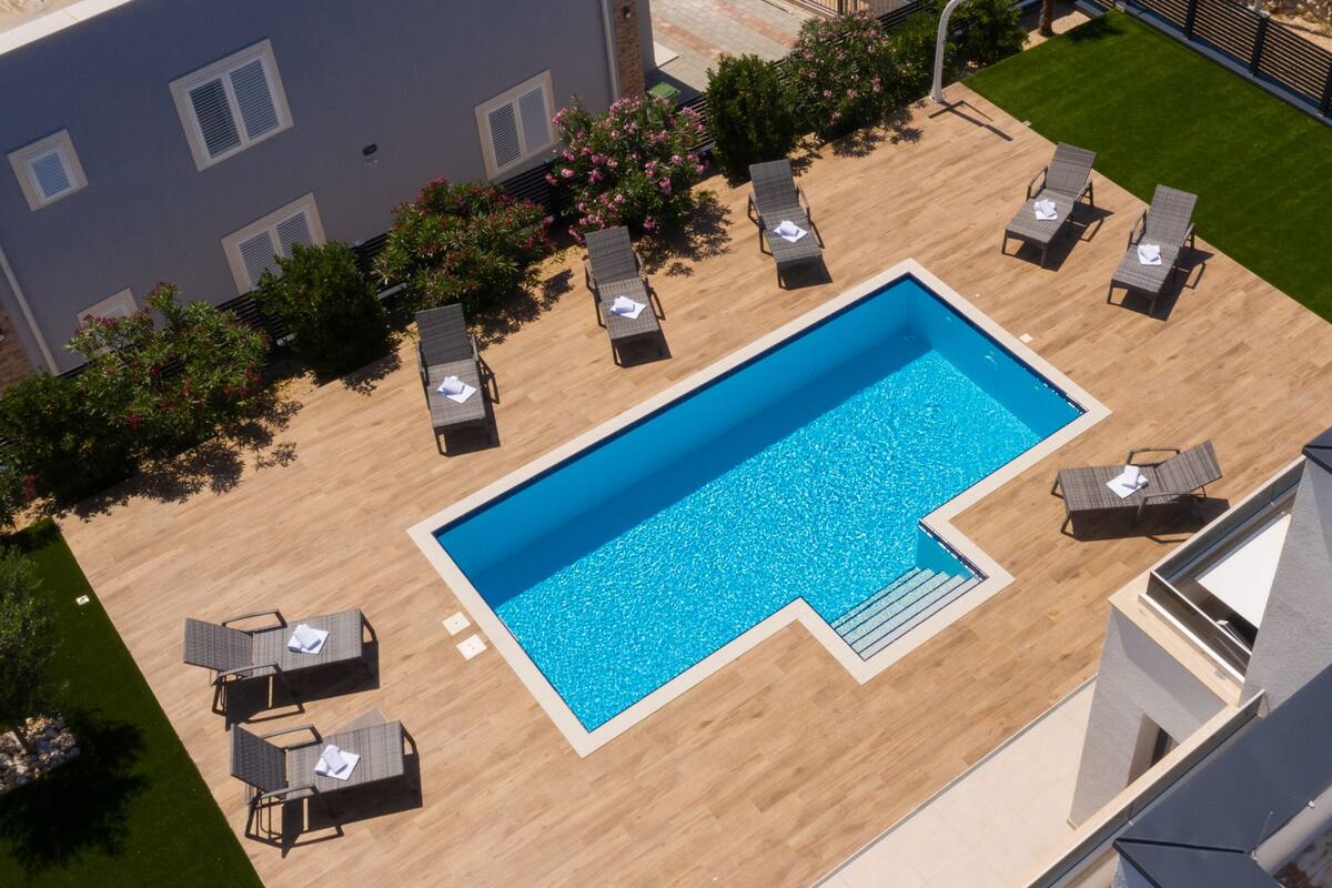 An aerial view of a rectangular swimming pool surrounded by lounge chairs and a wooden deck.