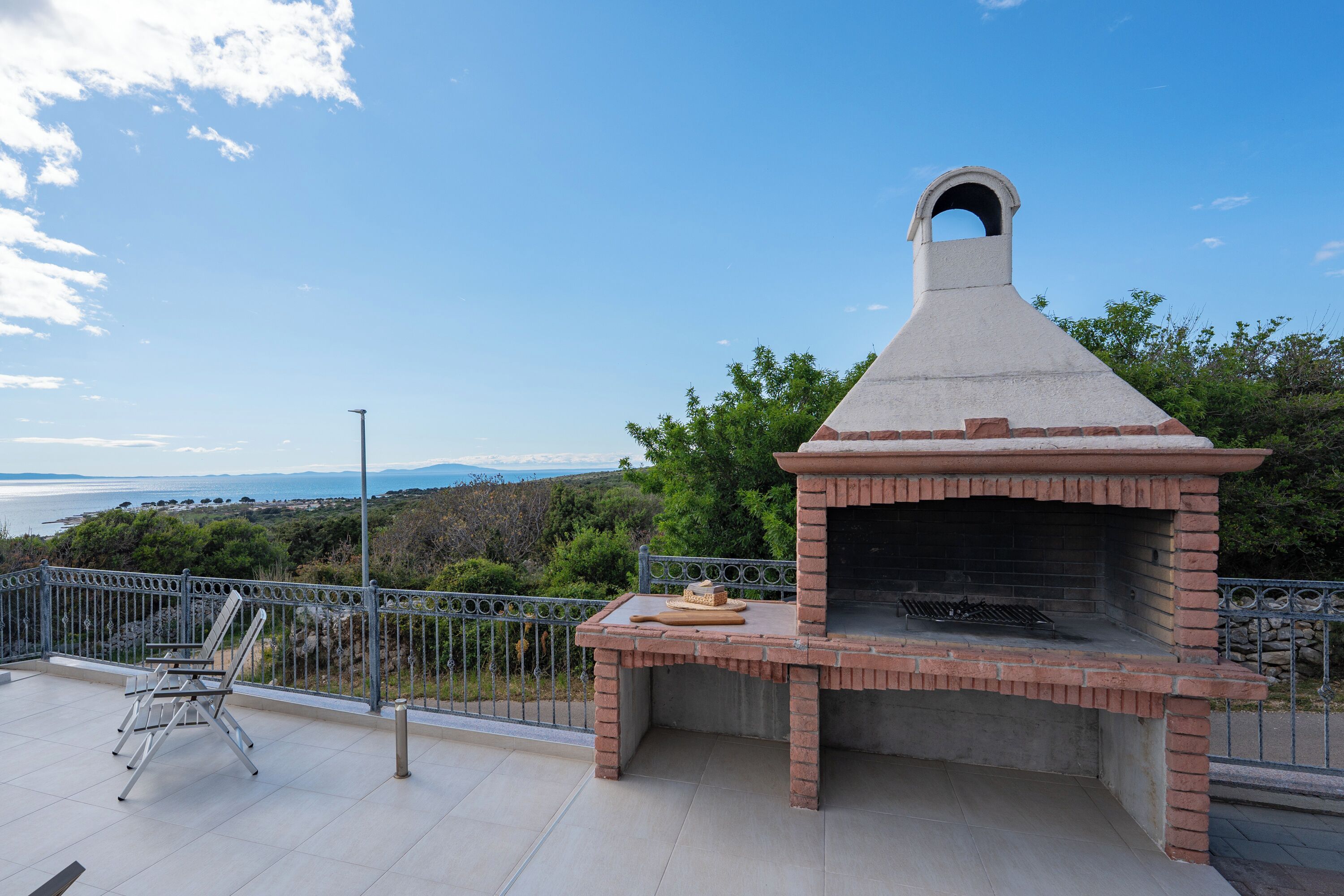 An outdoor brick oven with a chimney, a metal table with a hat and a cutting board, and a metal chair.