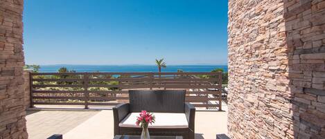 A patio with wicker furniture and a vase of flowers, overlooking a scenic view of the sea.