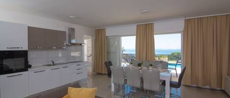 A modern kitchen with white cabinets, a built-in oven, and a dining area with a table and chairs.