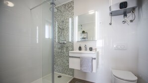 Ein modernes Badezimmer mit Duschkabine aus Glas, einem weißen Waschbecken mit Spiegel darüber und einer Toilette.