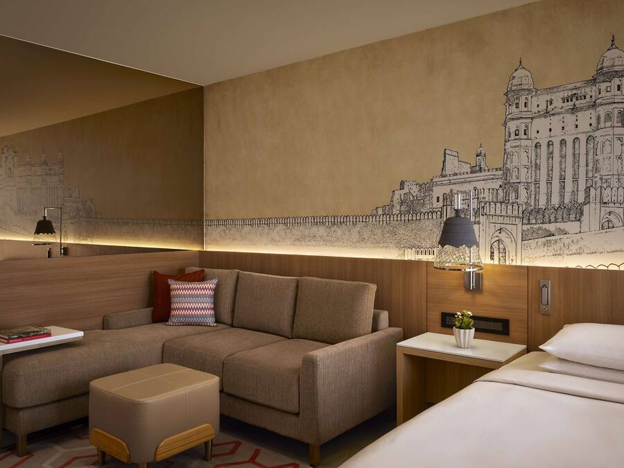 Una habitación de hotel moderna con un sofá grande, una mesita, una mesita de noche y una lámpara.